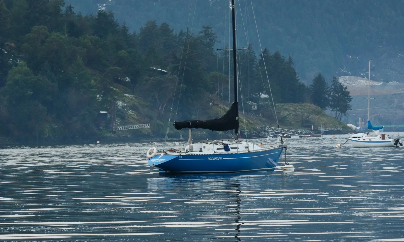 Voilier au mouillage dans une baie en hiver, collines enneigées en arrière-plan