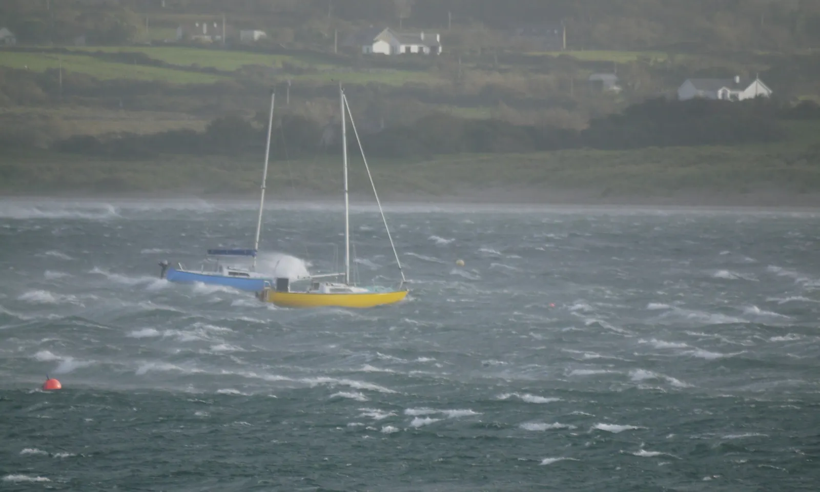 Voilier sous voilure réduite dans une mer grise et agitée, près d’une côte